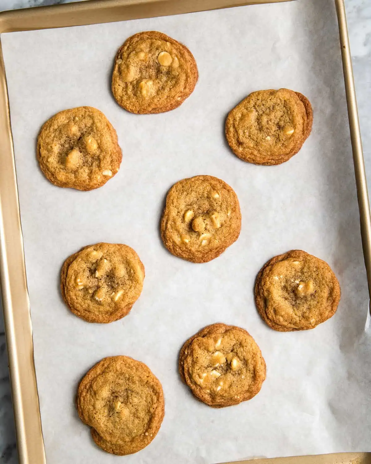 baked white chocolate chip cookies with walnuts cooling on a baking sheet.