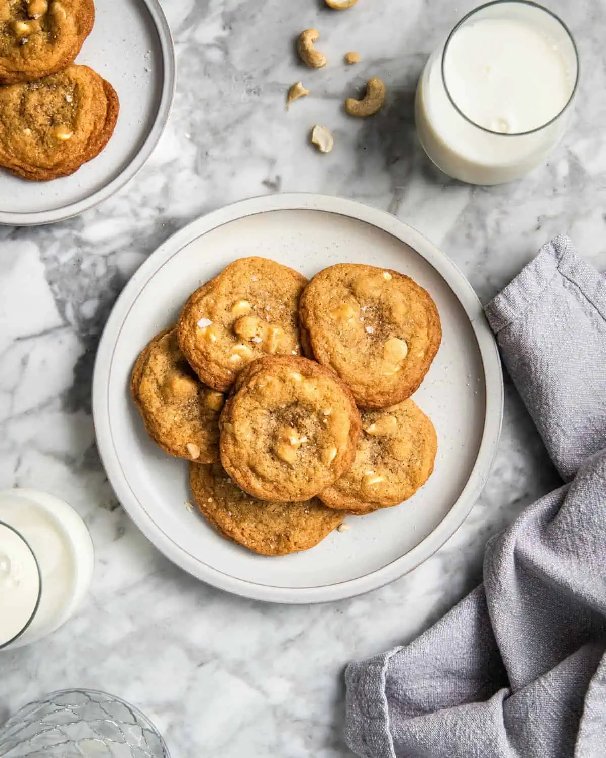 white chocolate chip cookies with cashews on a plate next to a glass of milk.
