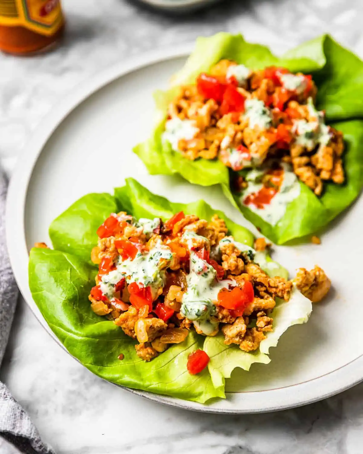 two lettuce wraps filled with ground chicken taco meat, tomatoes, and crema.