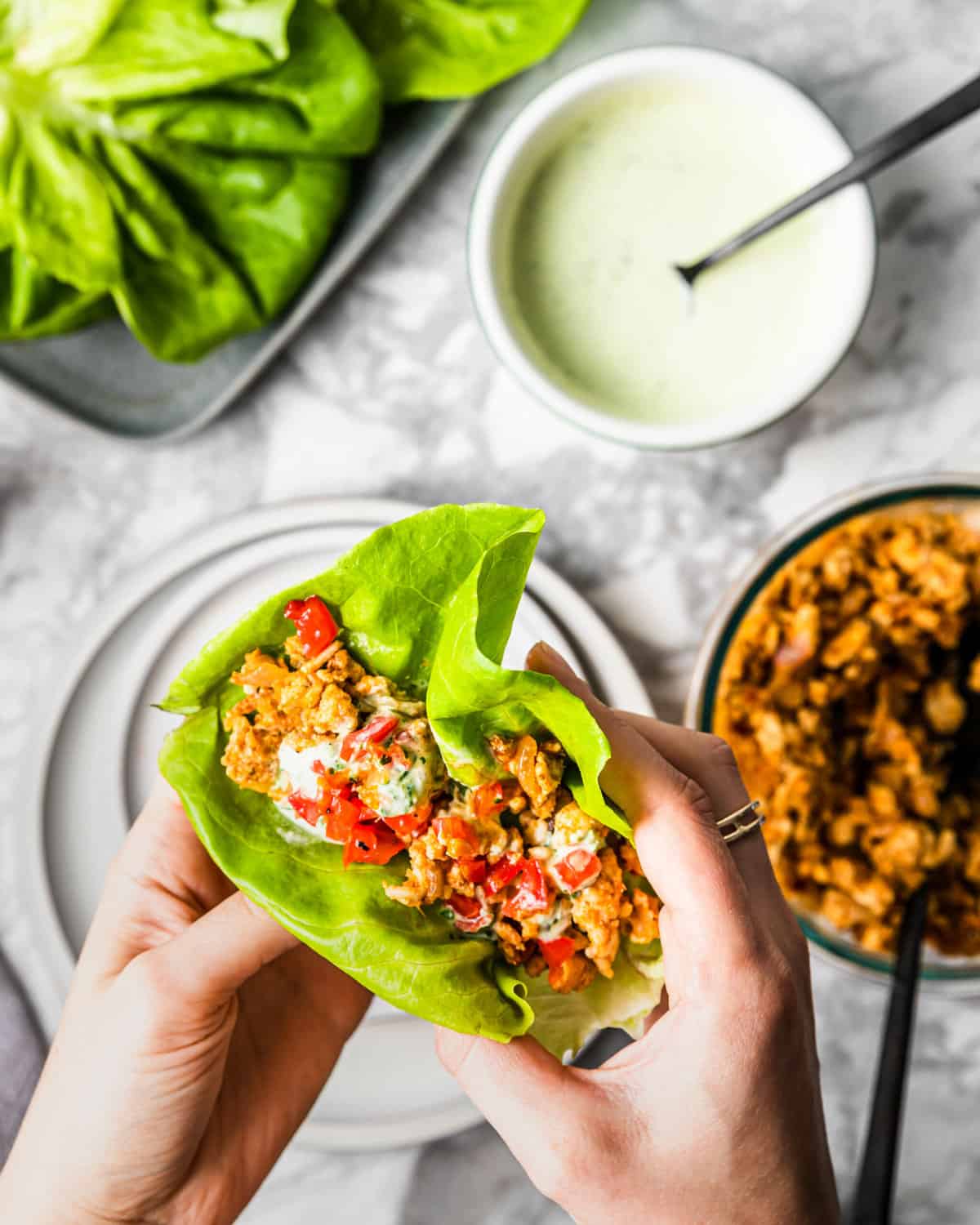 holding a lettuce wrap with ground mexican chicken with crema on top.