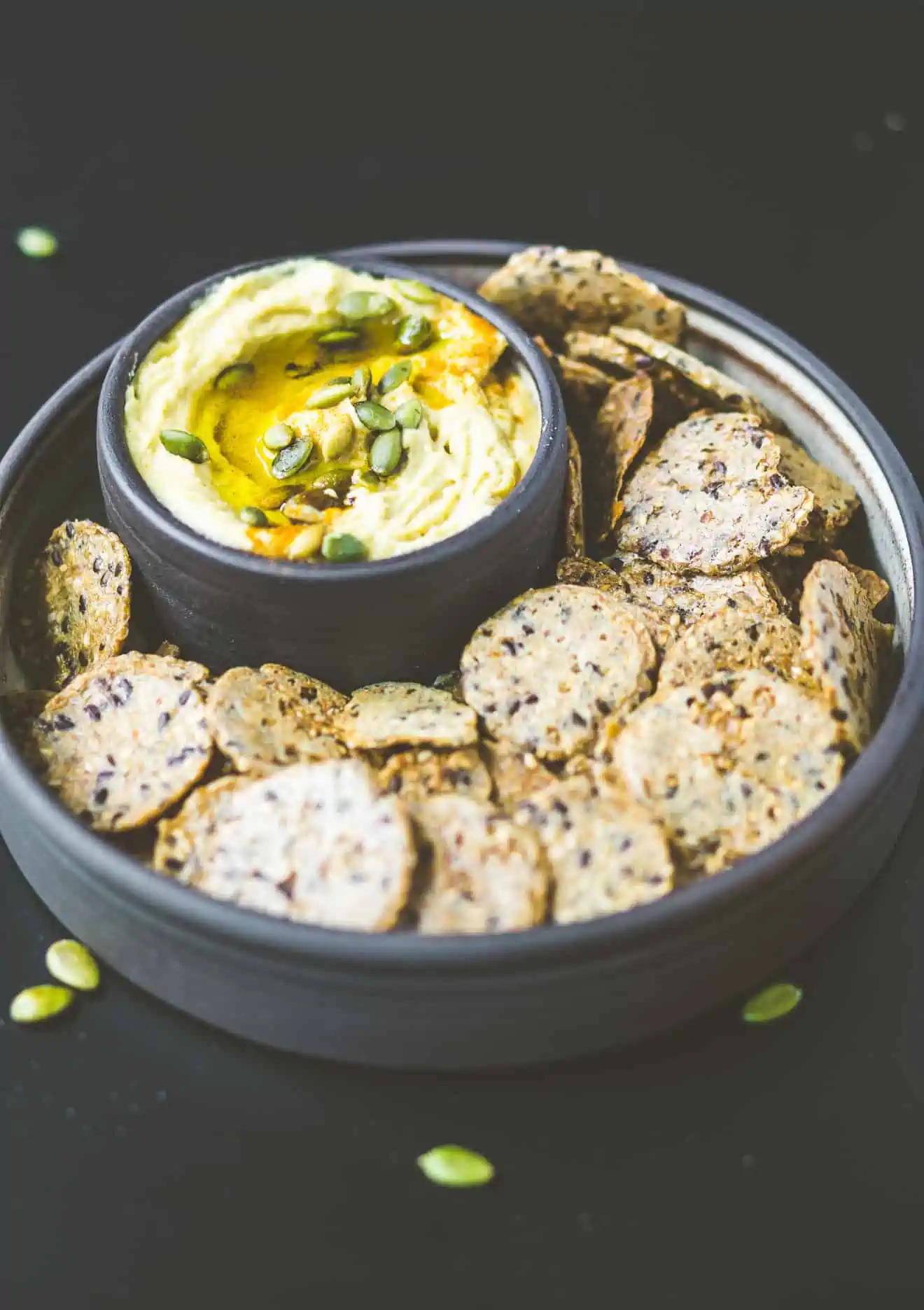 Pumpkin Hummus with crackers in a bowl with pumpkin seeds.