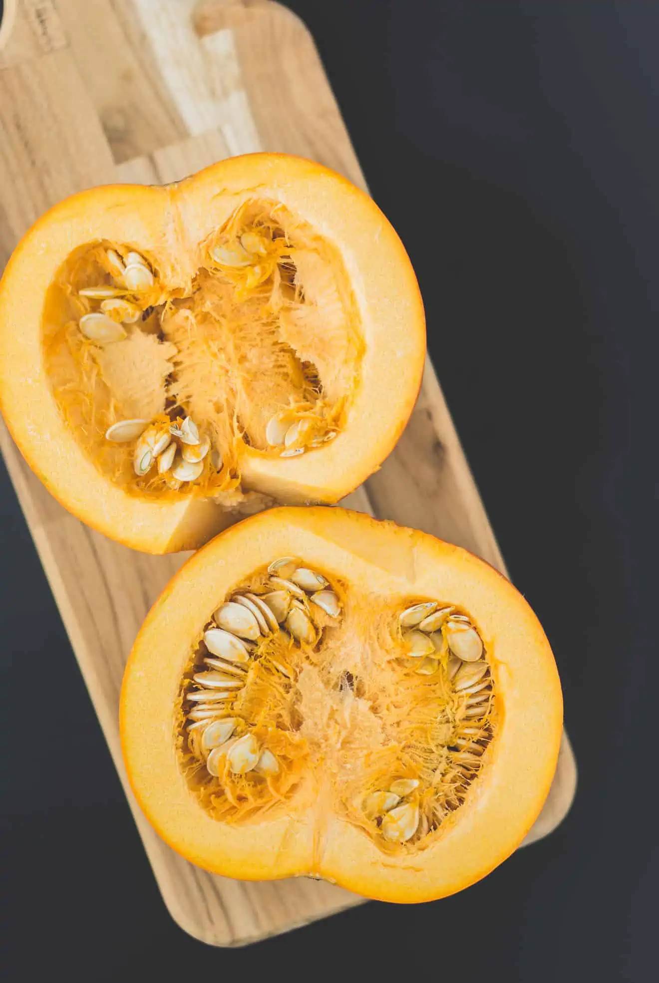 a small pumpkin cut in half with the seeds showing on a cutting board.
