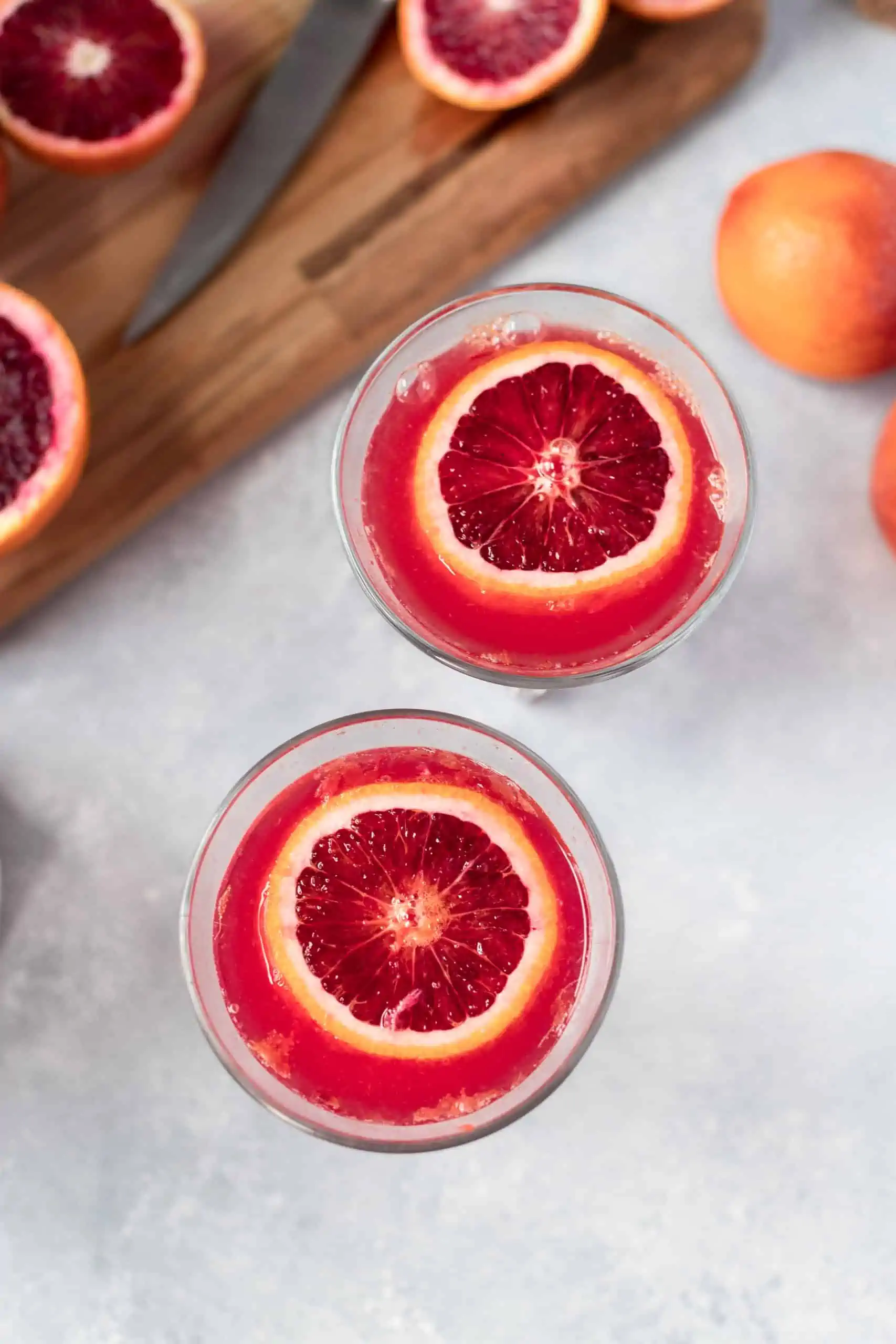 two glasses filled with blood orange juice and champagne and garnished with a sliced blood orange.