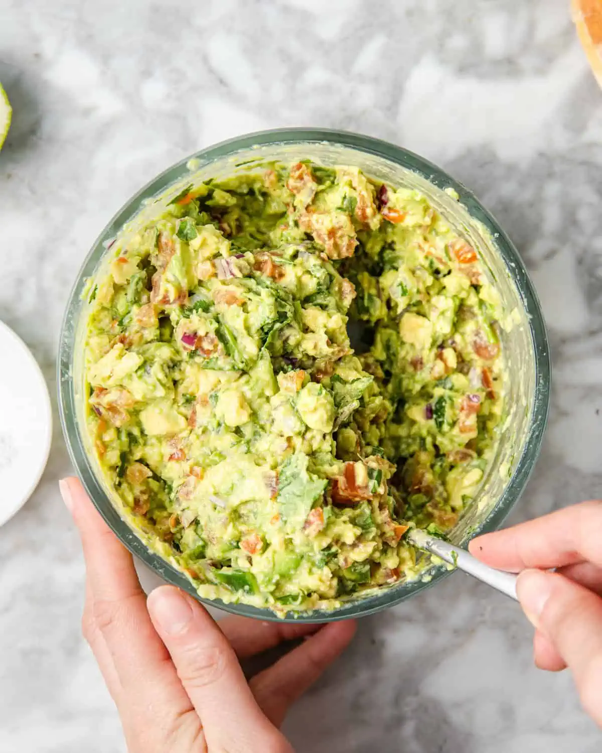 mixing smashed avocado with other salsa ingredients in a bowl on a counter.