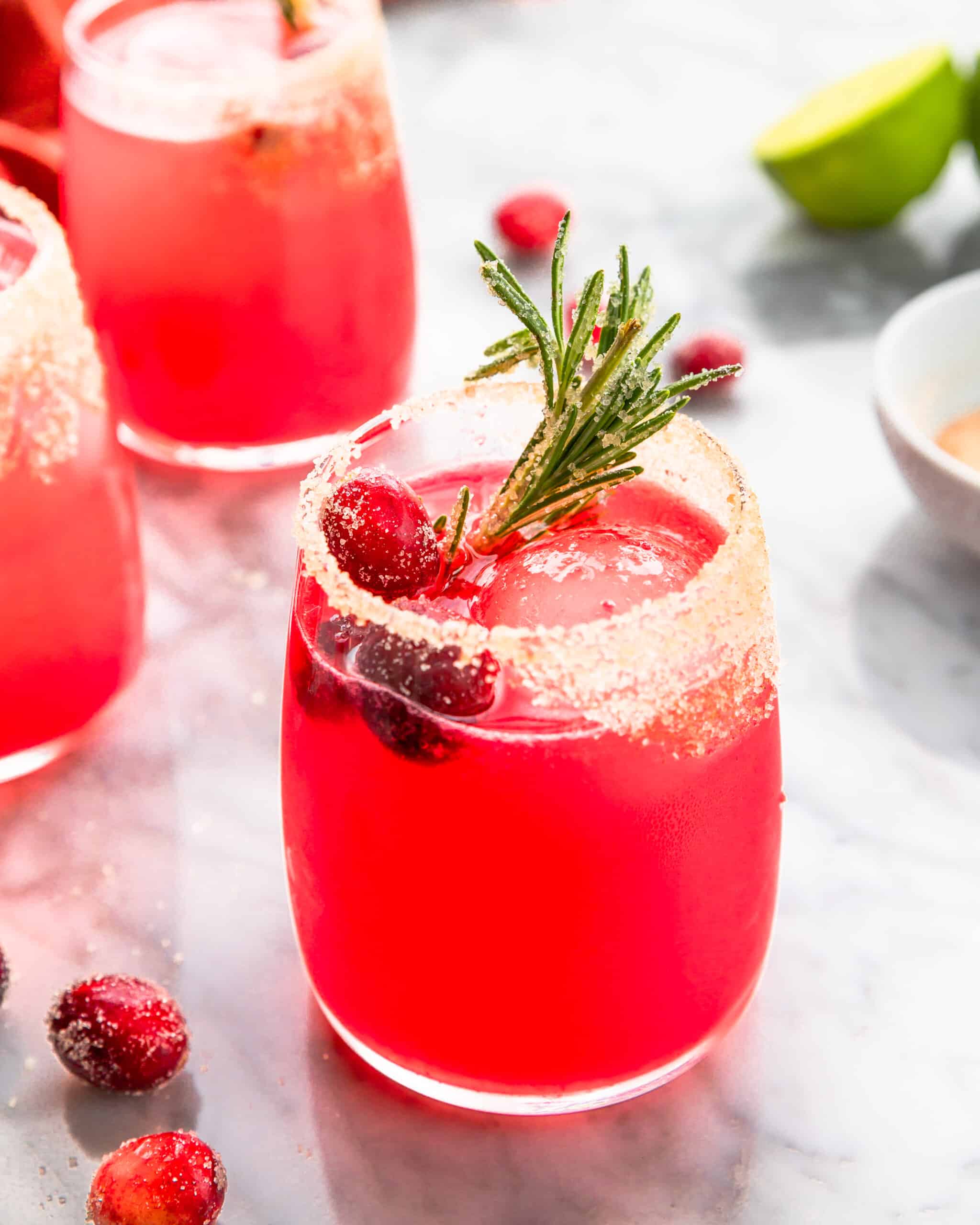 a glass of cranberry margarita with sugared rosemary.