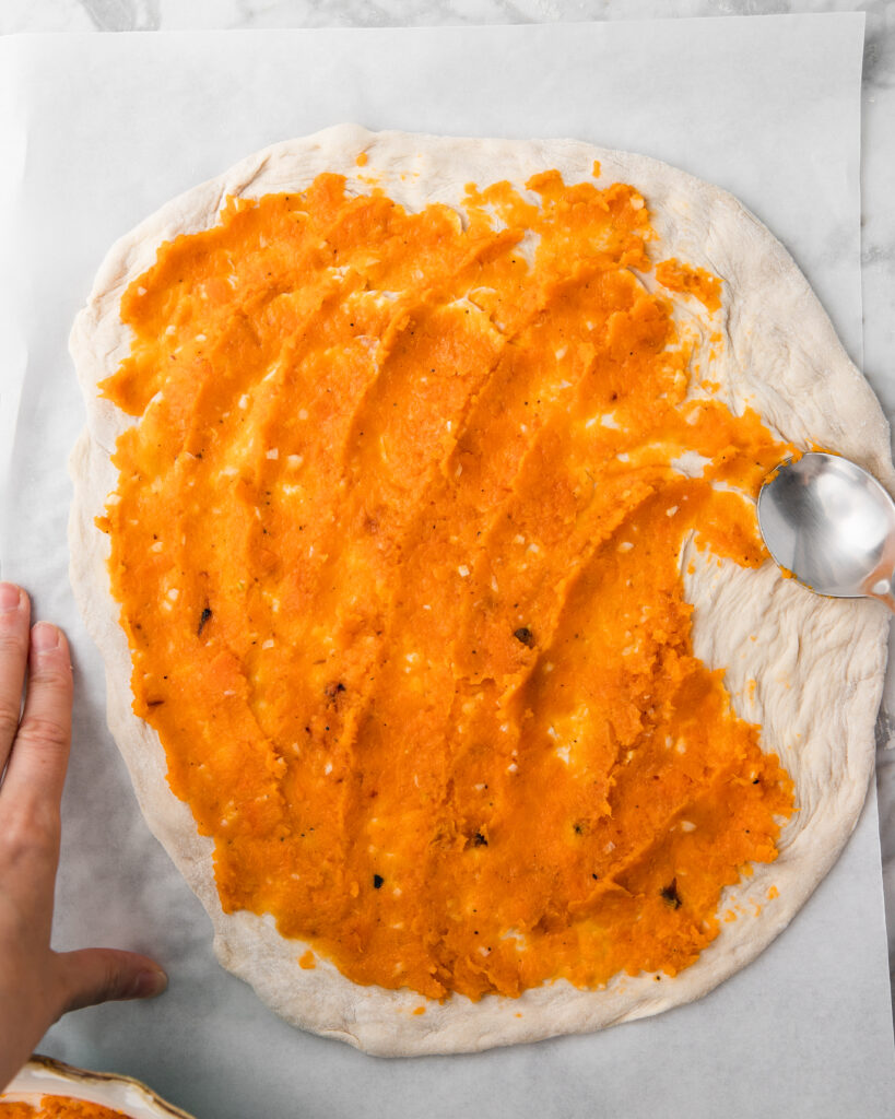 adding the mashed sweet potato to the pizza as a sauce.