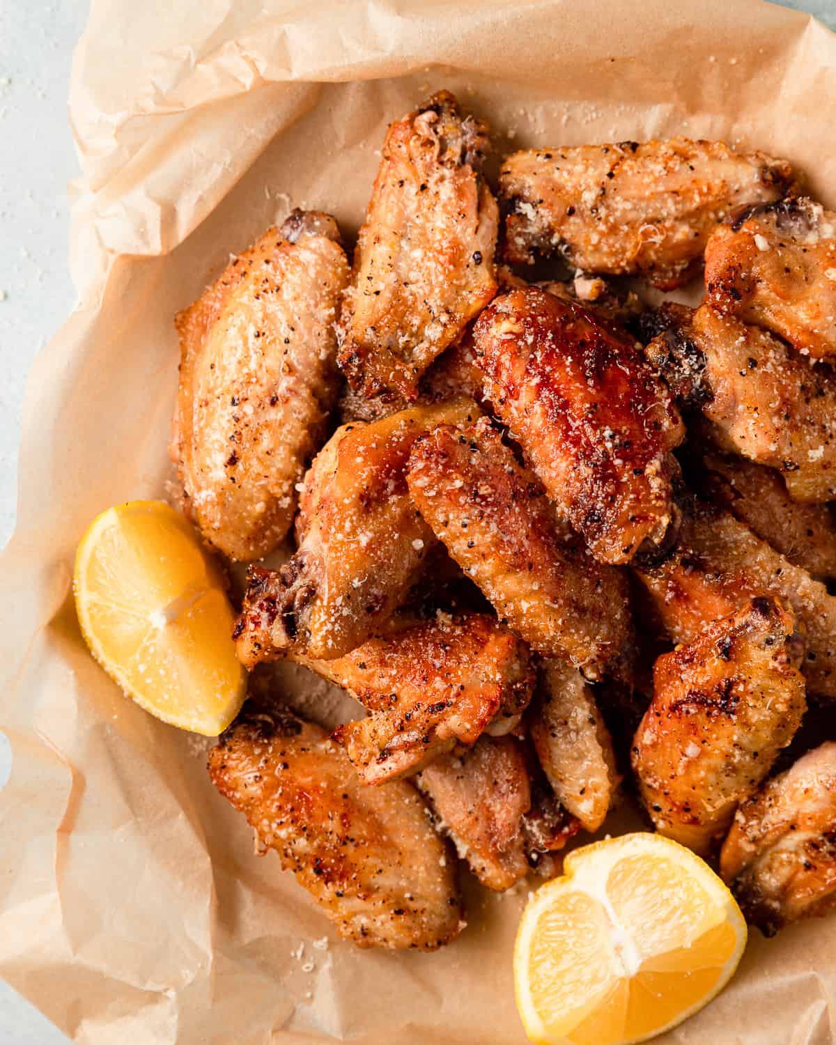 a bowl of baked wings with lemon wedges and parmesan cheese