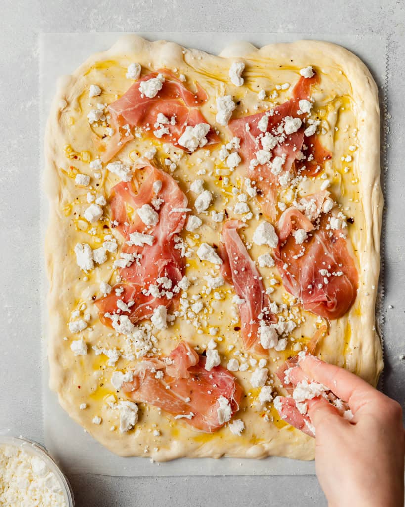 sprinkling goat cheese on pizza with prosciutto slices. 