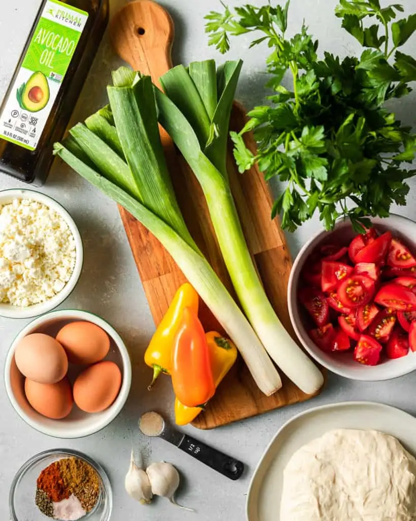 Shakshuka pizza ingredients: leeks, campari tomatoes, peppers, 4 eggs, feta cheese, spices, oil, parsley and pizza dough.