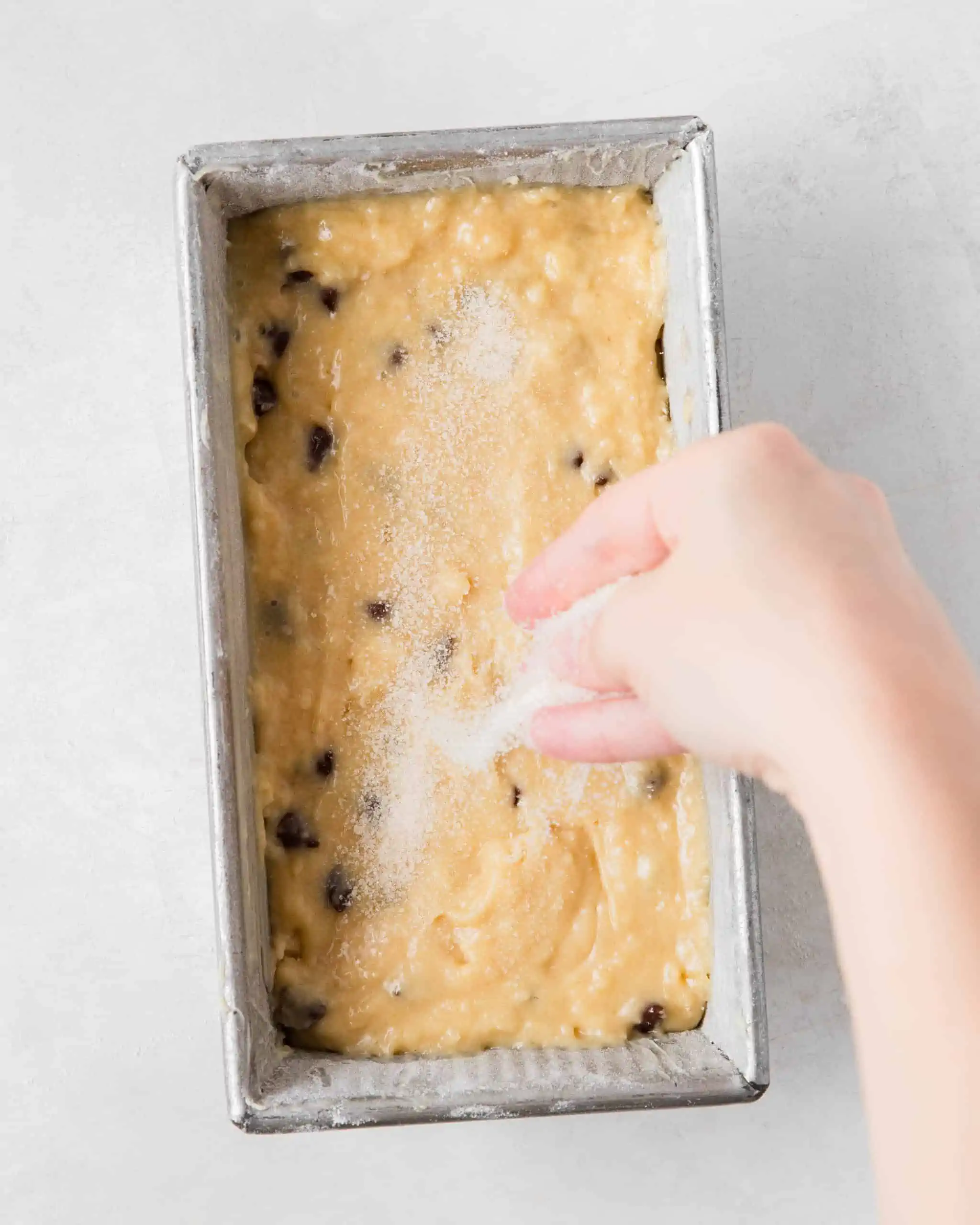 adding batter in loaf pan with sugar on top.