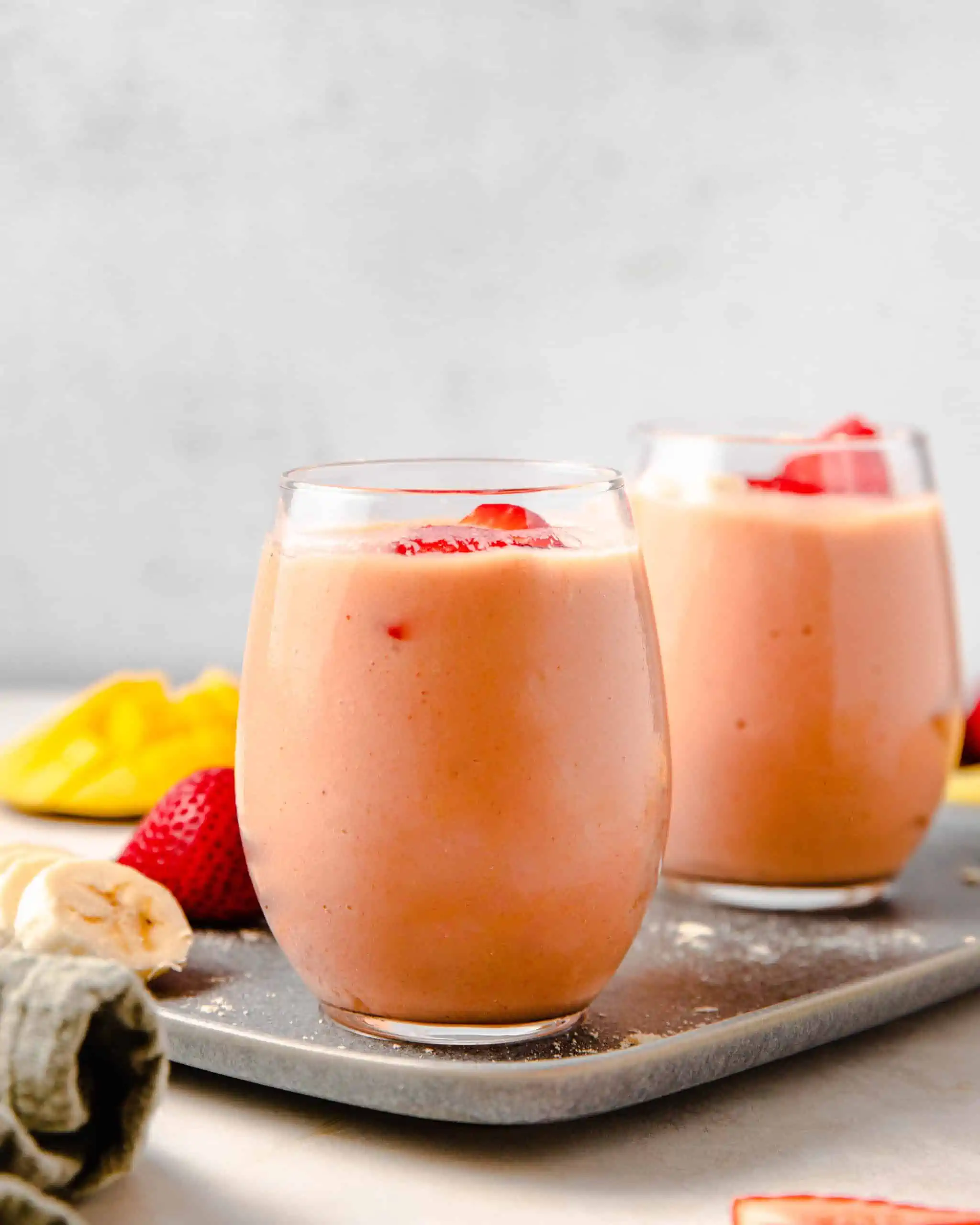 2 smoothie cups with fresh strawberries on top.