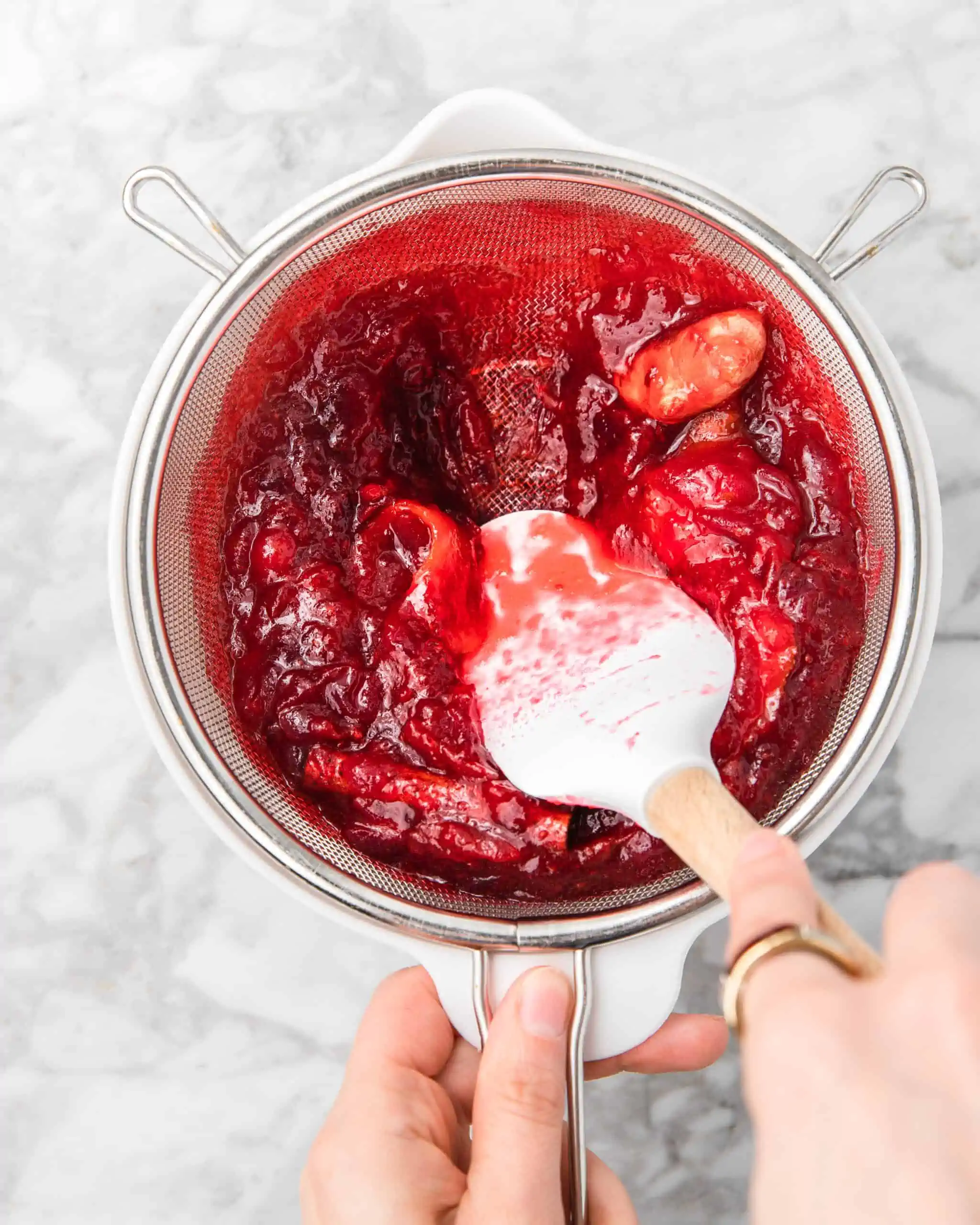 straining cranberry simple syrup in a bowl.