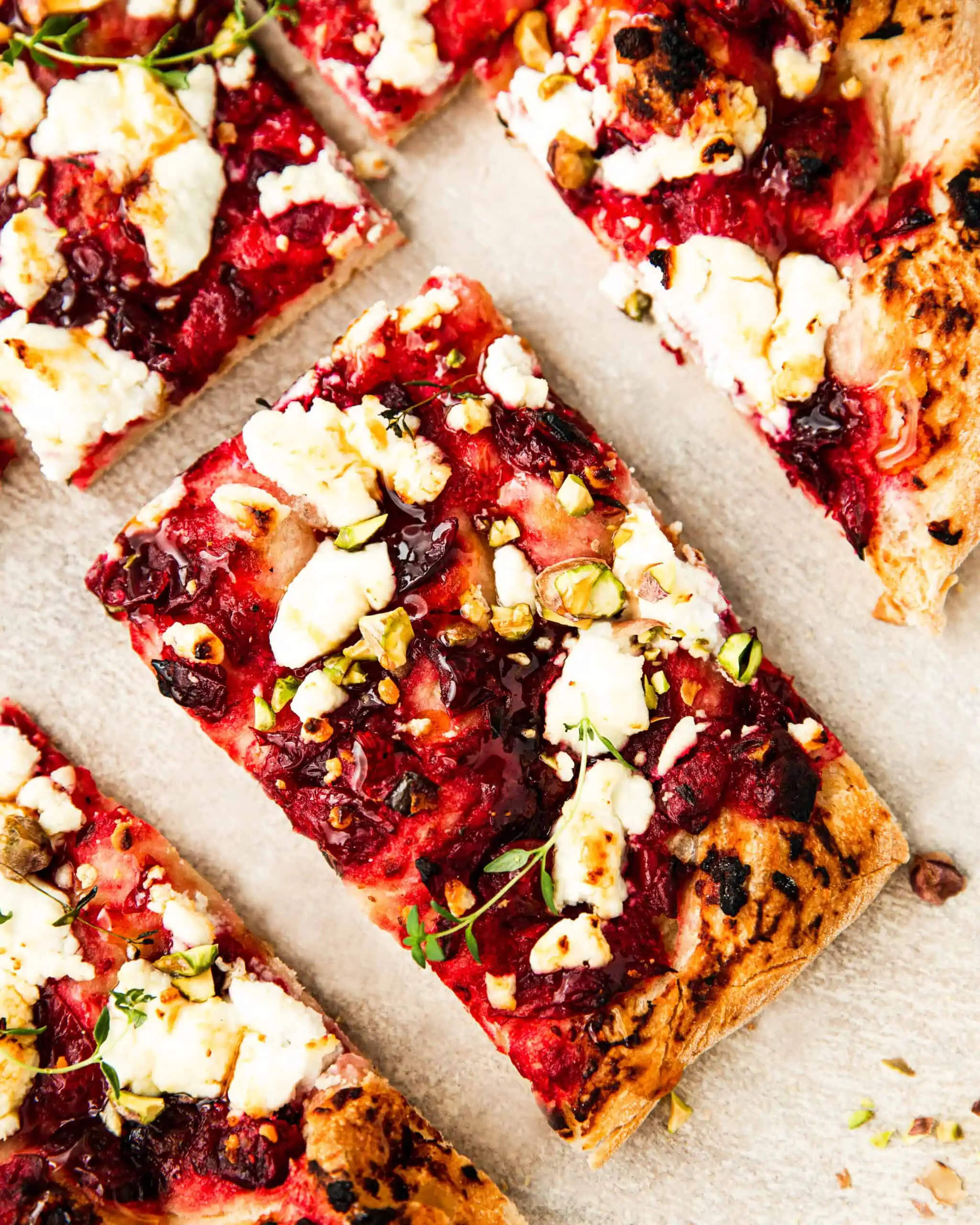 a slice of cranberry pizza with goat cheese, pistachios and honey on top.