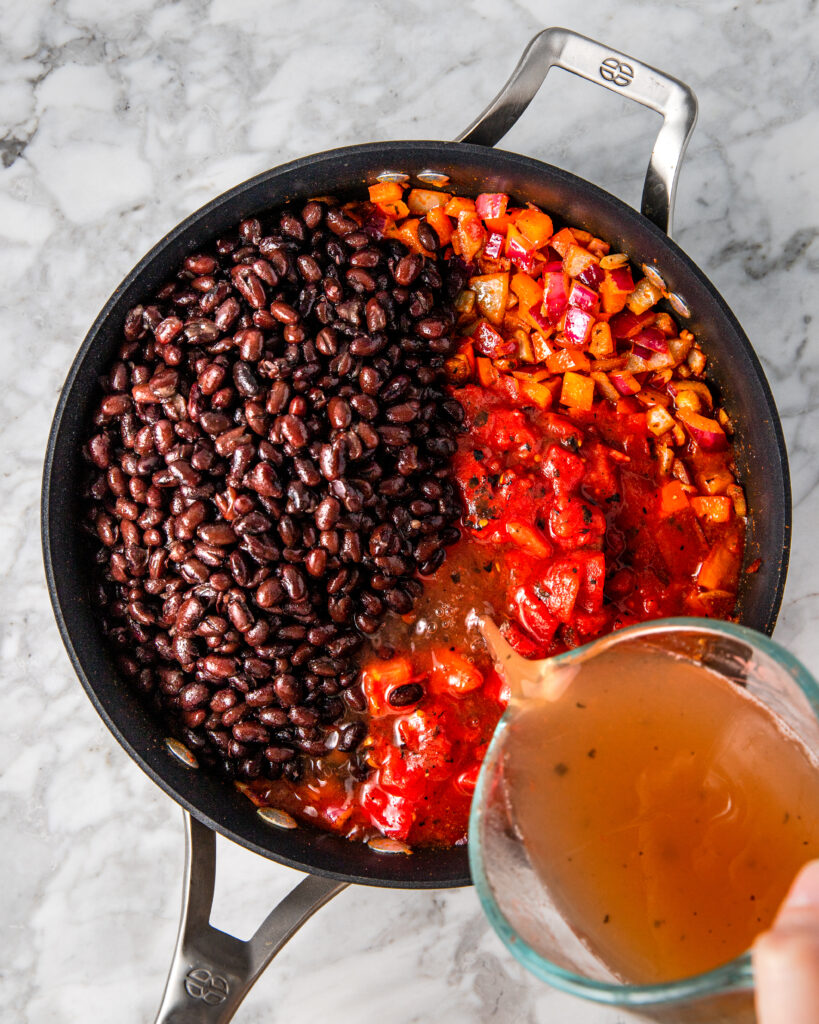 adding black beans and fire roasted tomatoes and broth to a pan.