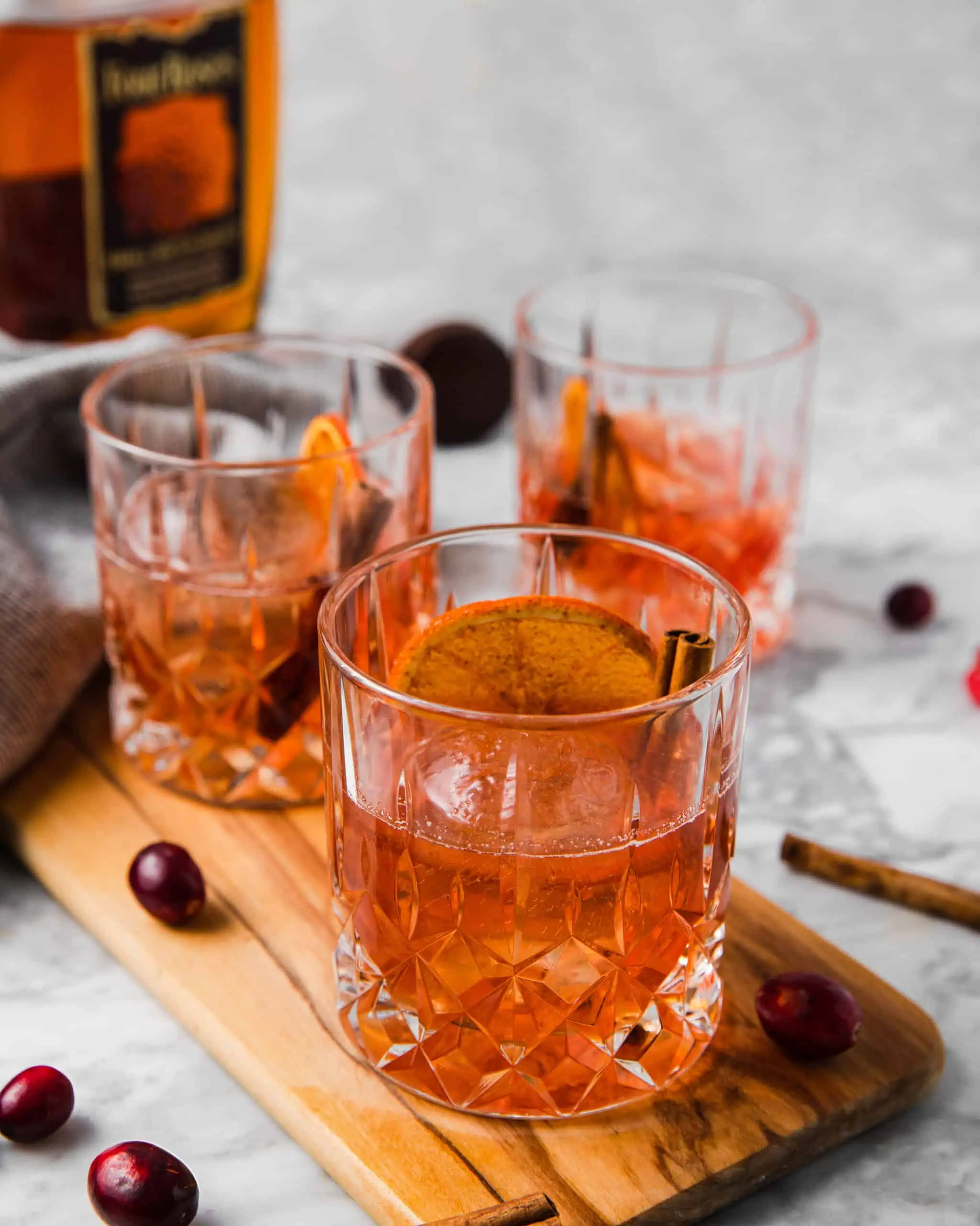 3 glasses of cranberry old fashioned with a orange wheel and cinnamon stick.