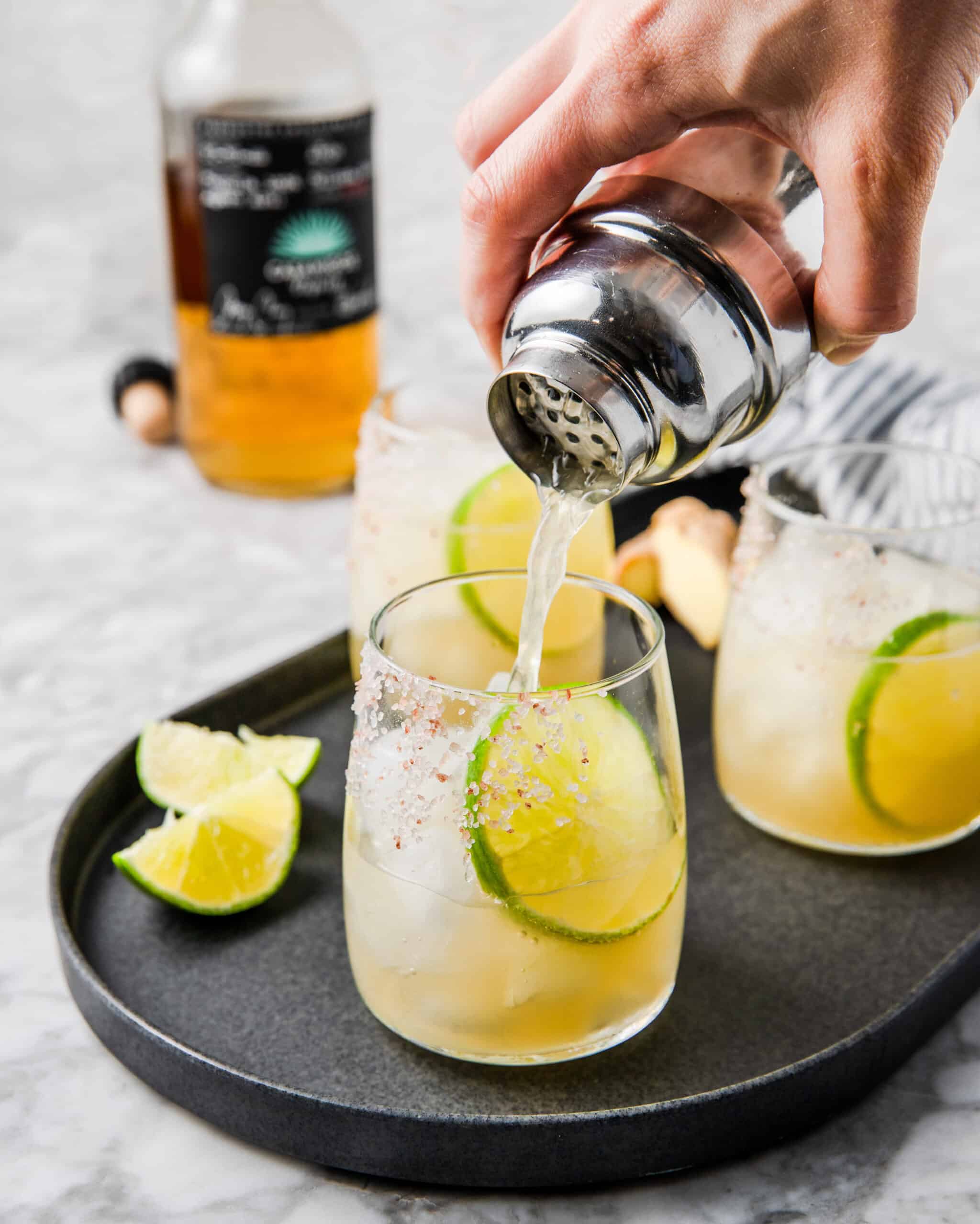 pouring ginger margarita in a glass with ice.