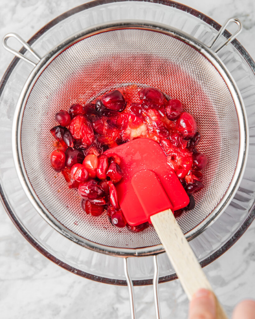 straining cranberry simple syrup over a bowl.