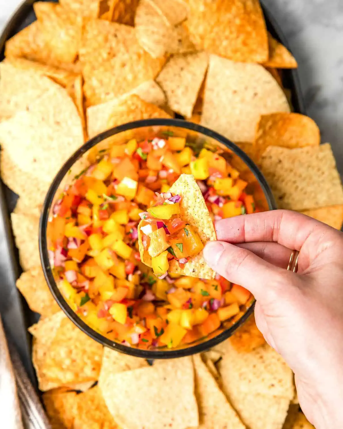 scooping out bell pepper salsa with a tortilla chip.
