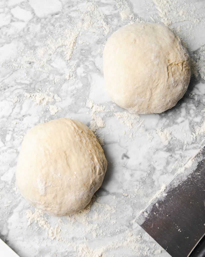 2 pizza dough balls divided on a counter.