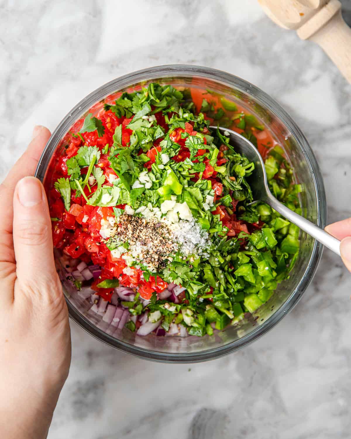 chopped salsa ingredients in a bowl being mixed by a spoon.