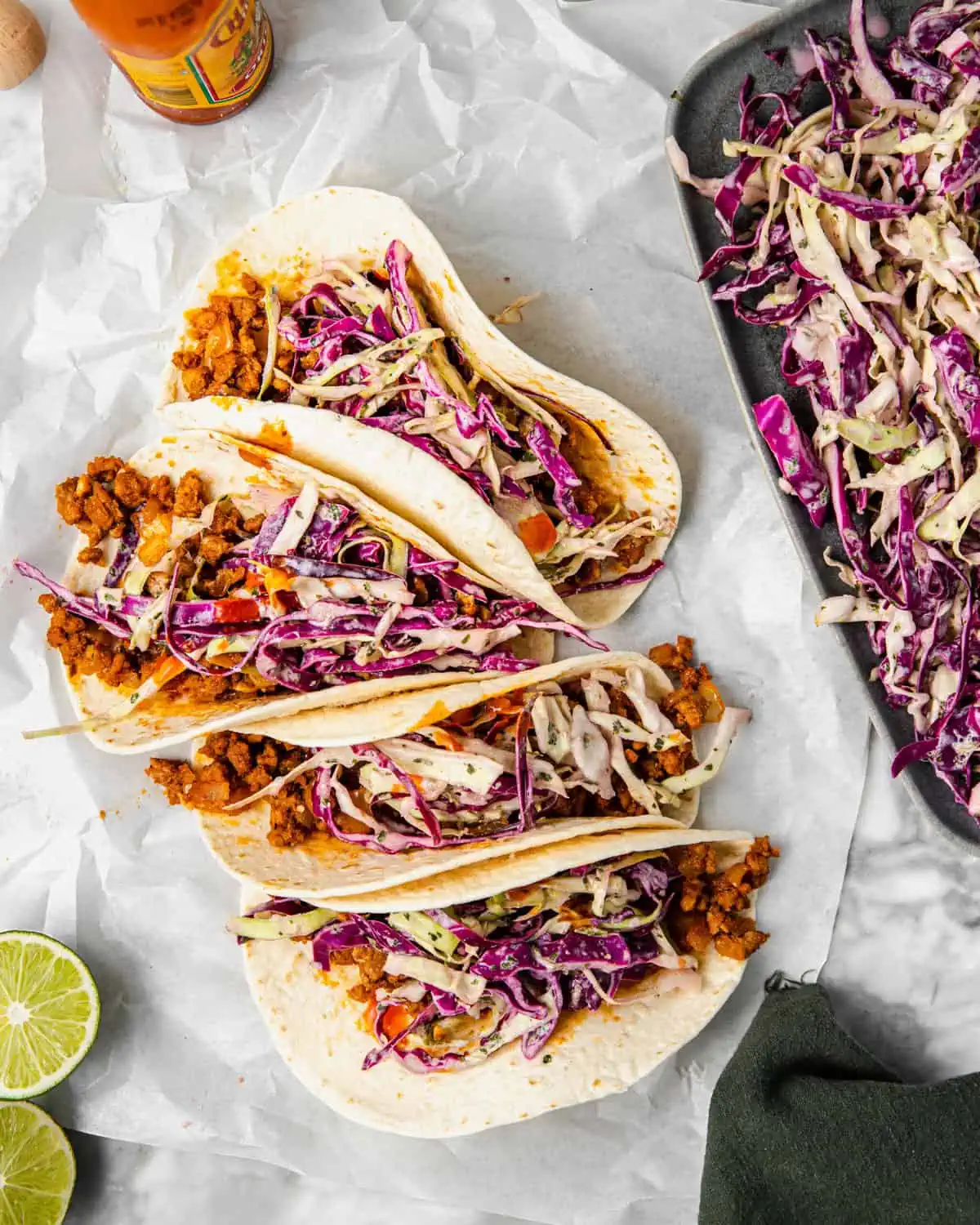 four pork tacos in a soft tortilla with cabbage slaw and hot sauce.