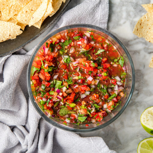a bowl of salsa fresca on a table with tortilla chips.